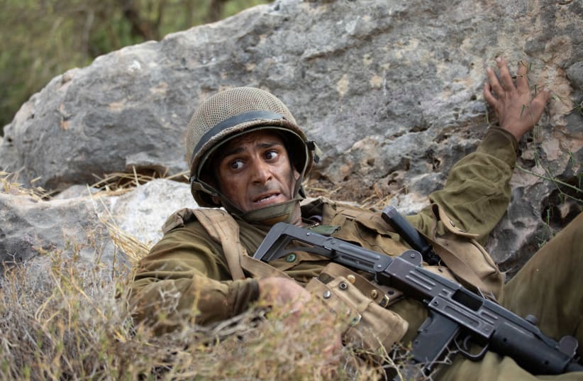 A Golani officer played by Aviv Alush is seen behind a rock in a promo for the Yom Kippur War drama 'Valley of Tears.' (photo credit: VERED ADIR/KAN 11)