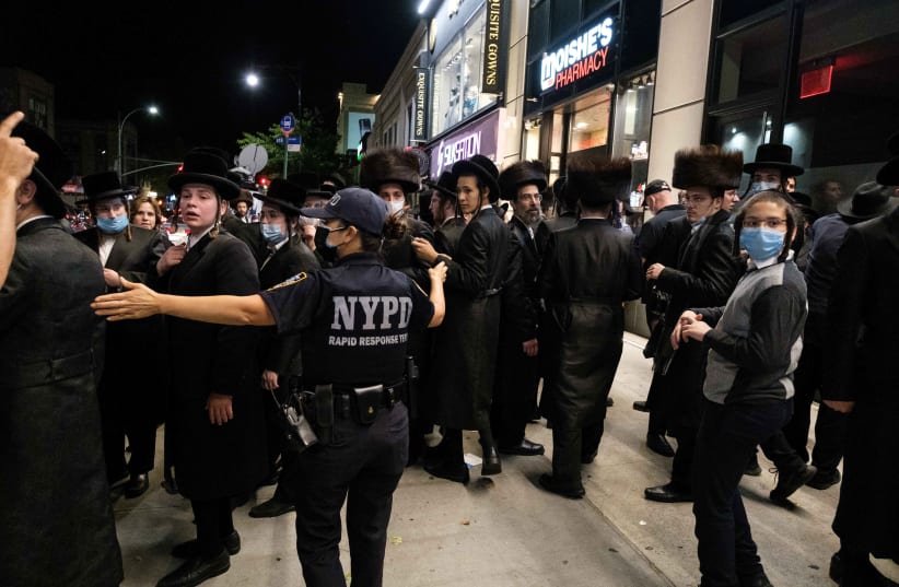 A NYPD officer speaks with Ultra-Orthodox Jews as they gather in the Borough Park neighborhood of Brooklyn amid the coronavirus outbreak in New York, US October 7, 2020 (photo credit: REUTERS/YUKI IWAMURA)