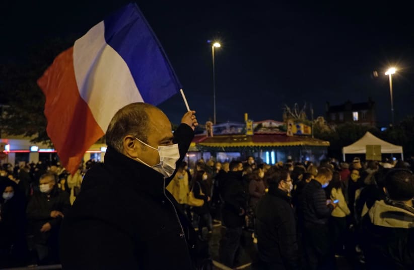 A man waves a French national flag during a silent march to pay tribute to Samuel Paty, the French teacher who was beheaded on the streets of the Paris suburb of Conflans-Sainte-Honorine, France, October 20, 2020 (photo credit: REUTERS/LUCIEN LIBERT)