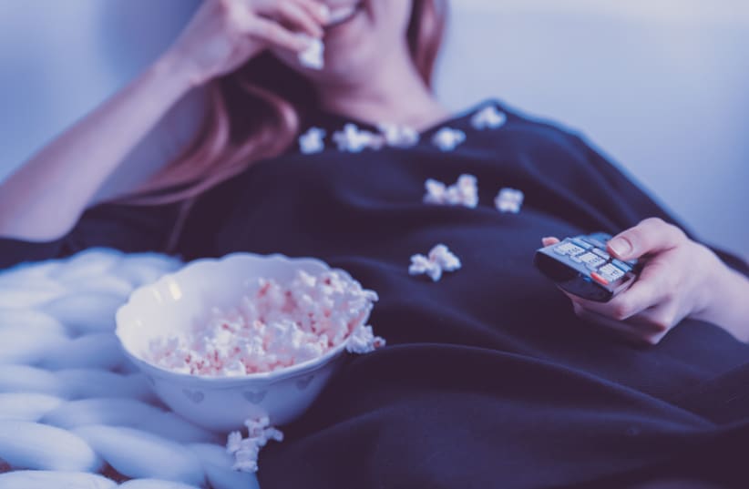 A woman eats popcorn while watching television.  (photo credit: PXFUEL)