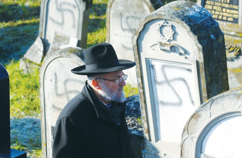 A MAN walks past gravestones desecrated with swastikas at the Jewish cemetery in Westhoffen, near Strasbourg, France, in December.  (photo credit: REUTERS)
