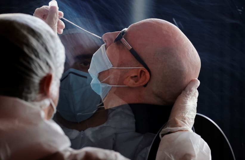 A health worker, wearing a protective suit and a face mask, administers a nasal swab to a patient in a temporary testing site for the coronavirus disease (COVID-19) at the Zenith Arena in Lille, France, October 26, 2020 (photo credit: REUTERS/PASCAL ROSSIGNOL)