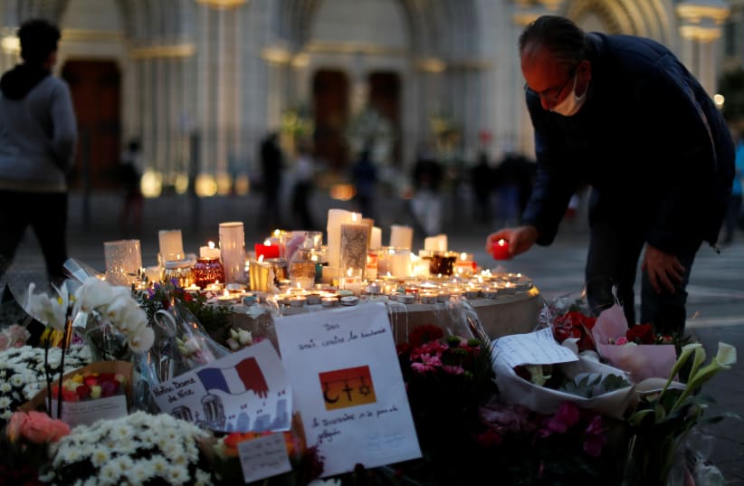 A man lights a candle near the Notre Dame church in tribute to the victims of a deadly knife attack in Nice, France, October 30, 2020 (photo credit: REUTERS/ERIC GAILLARD)