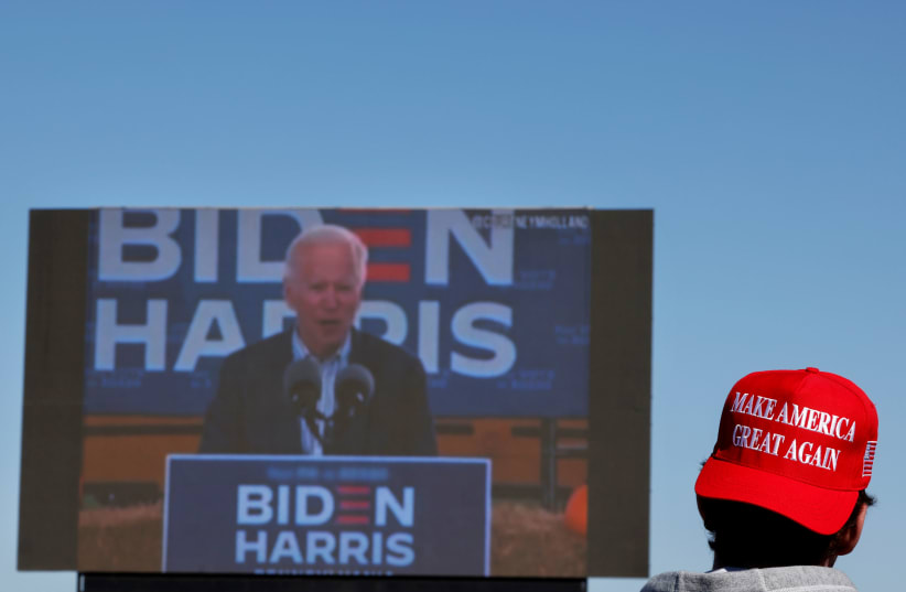 A person wearing a 'Make America Great Again' cap watches Democratic US presidential nominee Joe Biden (photo credit: REUTERS/CARLOS BARRIA)