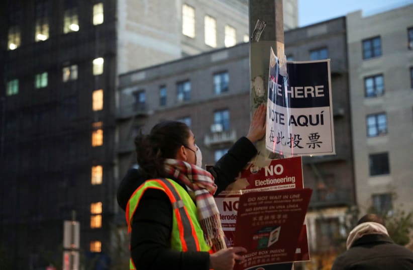 A worker tapes signs for voters before polls open, outside Brooklyn Public Library in New York, U.S., November 3, 2020. (photo credit: CAITLIN OCHS/REUTERS)