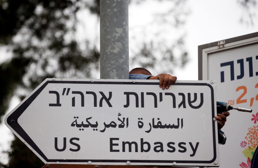 A worker hangs a road sign directing to the U.S. embassy, in the area of the U.S. consulate in Jerusalem, May 7, 2018.  (photo credit: REUTERS)