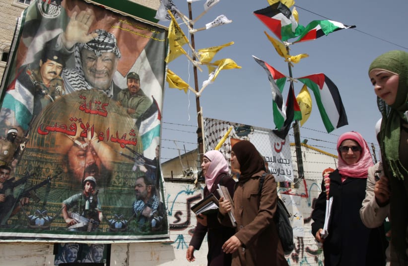 Palestinian students walk past a Fatah poster at the Palestine Polytechnic University in Hebron (photo credit: REUTERS)