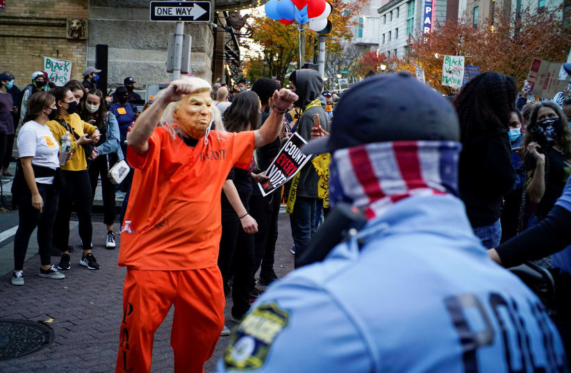 A person wears a mask depicting US President Donald Trump as supporters of U.S. presidential nominee Joe Biden take part in a rally as votes continue to be counted following the 2020 U.S. presidential election, in Philadelphia, Pennsylvania, U.S. November 6, 2020. (photo credit: REUTERS/EDUARDO MUNOZ)