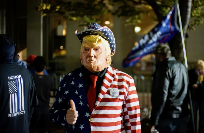 A supporter of US President Donald Trump dressed with the US flag colors and a mask depicting Trump gives a thumbs up as votes continue to be counted. November 6, 2020 (photo credit: EDUARDO MUNOZ / REUTERS)