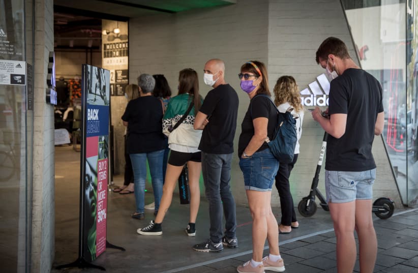 Israelis stand in line to enter clothing stores as shops officially opened after almost a 2-month long lockdown, November 08, 2020. (photo credit: MIRIAM ALSTER/FLASH90)