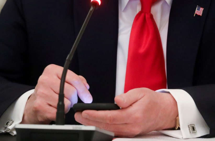 US President Donald Trump taps the screen on a mobile phone at the approximate time a tweet was released from his Twitter account, during a roundtable discussion on the reopening of small businesses in the State Dining Room at the White House in Washington, US, June 18, 2020. (photo credit: REUTERS/LEAH MILLIS/FILE PHOTO)