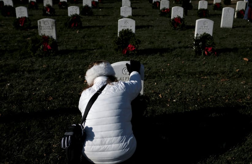 US Army combat veteran Marilyn Pietri of Woodbridge, Virginia places her hand on a headstone as she lays a Christmas wreath at Arlington National Cemetery in Arlington, Virginia, US, December 16, 2017. (photo credit: REUTERS/JAMES LAWLER DUGGAN)