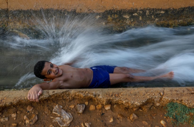 Double duty. An irrigation canal provides a place for a Palestinian boy to cool off in September near the West Bank city of Jericho. (photo credit: (AHMAD GHARABLI/AFP VIA GETTY IMAGES))