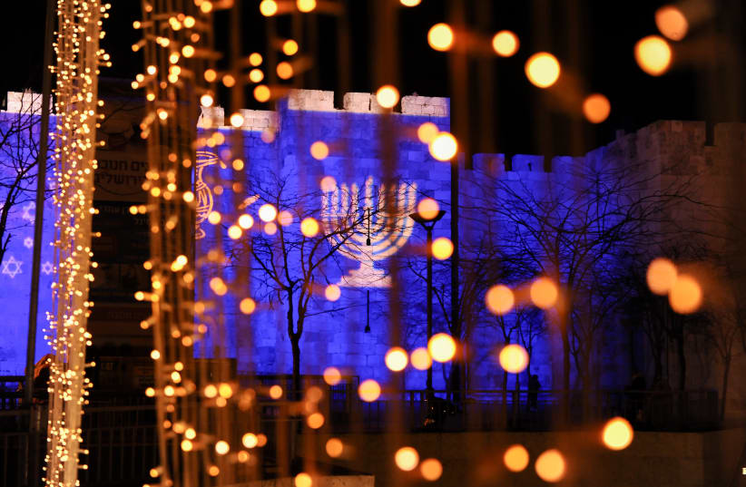 A symbol of a 'chanuckia', used during the Jewish holiday of Hanukkah, is displayed on the Old City walls of Jerusalem, on December 12, 2015. Hanukkah, also known as the Festival of Lights, is an eight-day Jewish holiday commemorating the rededication of the Holy Temple. The festival is observed by  (photo credit: MENDY HECHTMAN/FLASH90)