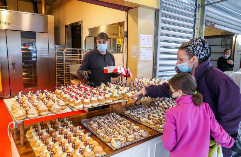 Israelis are seen buying donuts ahead of Hanukkah at the Marzipan bakery near Mahane Yehuda in Jerusalem, wearing masks in accordance with coronavirus restrictions, on December 6, 2020. (photo credit: MARC ISRAEL SELLEM/THE JERUSALEM POST)