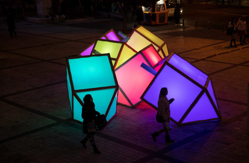 People walk by large lit up "sevivons", placed in Jerusalem, for the Jewish holiday of Hanukkah. The sevivon (dreidel) is a four-sided spinning top traditionally played with during Hanukkah, December 24, 2019. (photo credit: YONATAN SINDEL/FLASH90)