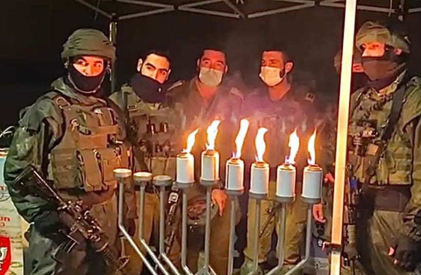 Soldiers in the IDF's Netzah Yehuda battalion are seen lighting Hanukkah candles at the Givat Assaf junction, where two of its members were murdered and a third wounded in a terrorist attack in 2018. (photo credit: NETZAH YEHUDAH)