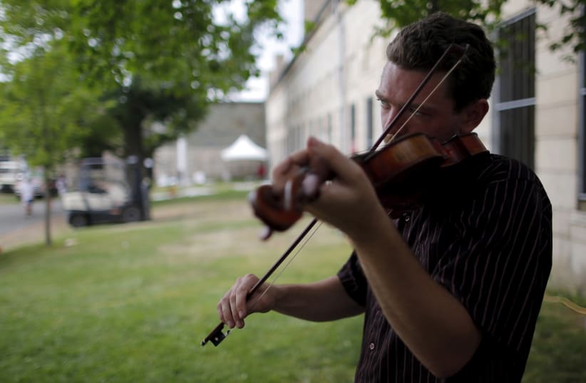        The Downhill Strugglers’ Jackson Lynch plays a fiddle backstage at the Newport Folk Festival in Rhode Island. The book traces the impact of a family fiddle passed down through multiple generations.  (photo credit: BRIAN SNYDER / REUTERS)