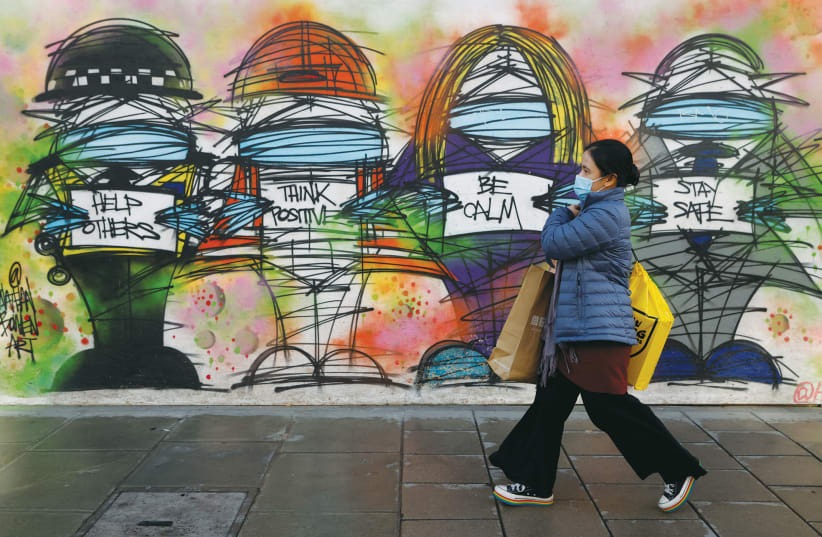 A woman wearing a face mask walks past coronavirus-related graffiti in central London in October. (photo credit: REUTERS/JOHN SIBLEY)