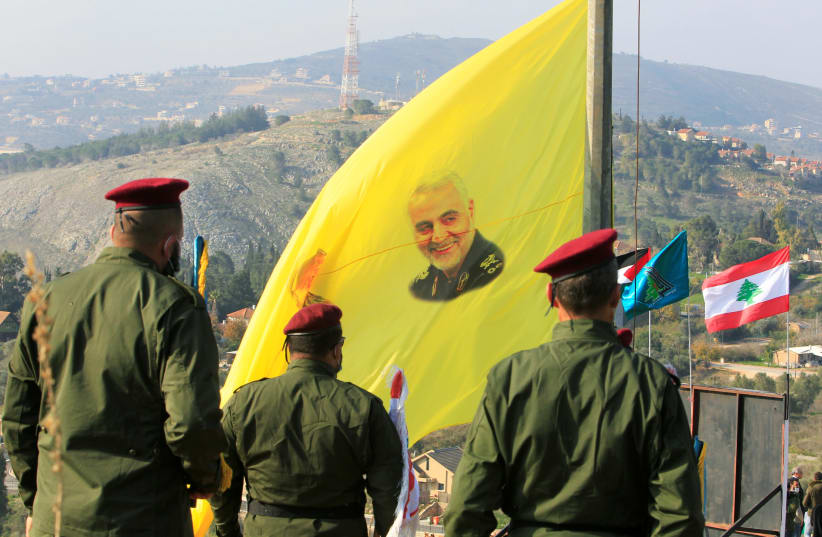 Members of Lebanon's Hezbollah stand near a flag with a picture of senior Iranian military commander General Qassem Soleimani, during a ceremony marking the first anniversary of the killing of Soleimani and Iraqi militia commander Abu Mahdi al-Muhandis in a US attack, in the southern Lebanese villag (photo credit: REUTERS/AZIZ TAHER)