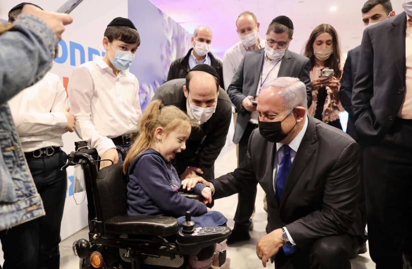 Prime Minister Benjamin Netanyahu is seen with young Ila Schwartz at the Meuhedet coronavirus vaccine center, on January 6, 2021. (photo credit: MARC ISRAEL SELLEM/THE JERUSALEM POST)