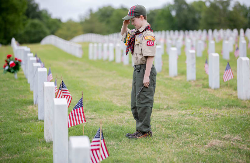 Cub Scout Colten Short, 10, of Arlington, salutes a grave after fixing a flag in front of a headstone ahead of the Memorial Day weekend at West Tennessee State Veterans Cemetery in Memphis, Tennessee, US May 19, 2020. (photo credit: MAX GERSH/THE COMMERCIAL APPEAL/USA TODAY NETWORK VIA REUTERS)