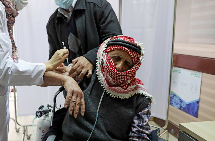 A Palestinian man is helped by his son as he receives a vaccination against the coronavirus disease (COVID-19) as Israel continues its national vaccination drive, in east Jerusalem December 23, 2020 (photo credit: REUTERS/AMMAR AWAD)