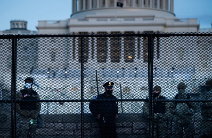 A Capitol police officer stands with members of the National Guard behind a crowd control fence surrounding Capitol Hill a day after a pro-Trump mob broke into the Capitol building, Jan. 7, 2021 (photo credit: BRENDAN SMIALOWSKI/AFP VIA GETTY IMAGE)