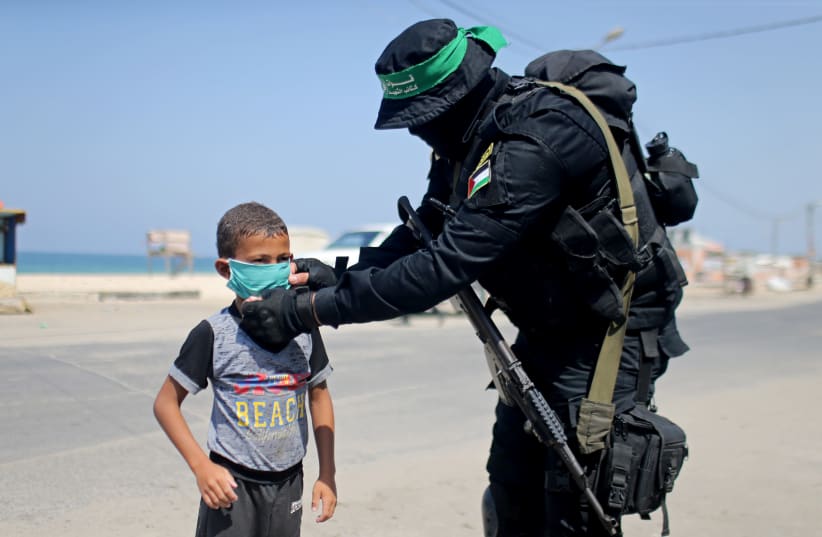 A Hamas militant hands out a protective face mask to a Palestinian boy during the coronavirus disease (COVID-19) outbreak, in the central Gaza Strip September 12, 2020. (photo credit: IBRAHEEM ABU MUSTAFA / REUTERS)