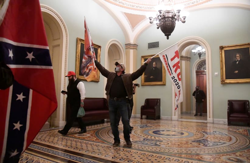 A supporter of US President Donald Trump waves Trump and Confederate flags after making his way to the second floor of the US Capitol during the insurrection on January 6. (photo credit: MIKE THEILER/REUTERS)