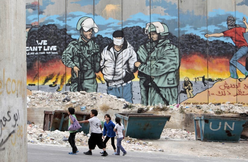 Children walk in front of a mural painted on part of Israel’s security barrier at the Aida refugee camp in Bethlehem. (photo credit: AMMAR AWAD/REUTERS)
