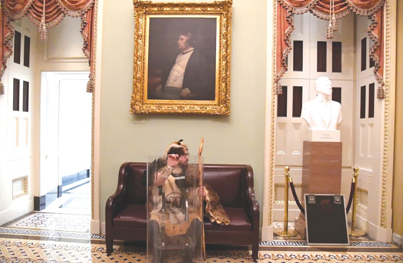 AARON MOSTOFSKY, a supporter of US President Donald Trump, takes a seat away from the action on the second floor of the US Capitol near the entrance to the Senate after breaching security defenses last week. (photo credit: MIKE THEILER/REUTERS)