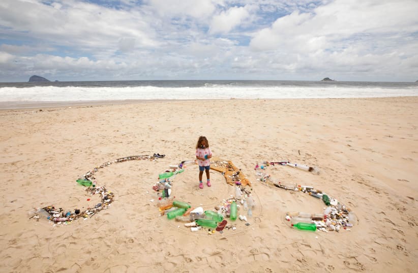 A young girl stands with collected trash sign reading SOS (photo credit: RICARDO GOMES/REUTERS)