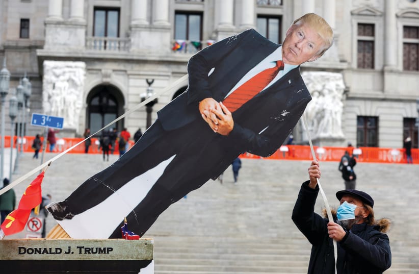 A MAN topples a cardboard cutout depicting former president Donald Trump outside the Pennsylvania State Capitol in Harrisburg, Pennsylvania, on Sunday. (photo credit: RACHEL WISNIEWSKI/REUTERS)