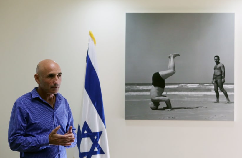 Ofer Shelah stands next to photographer Paul Goldman’s iconic image of David Ben-Gurion doing a handstand at the Tel Aviv beach in 1957. (photo credit: MARC ISRAEL SELLEM)
