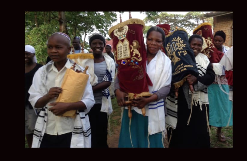 Women and children carry Torah scrolls from an old synagogue building to a new building in Nabagoye, Ugandaz (photo credit: COURTESY BE’CHOL LASHON)