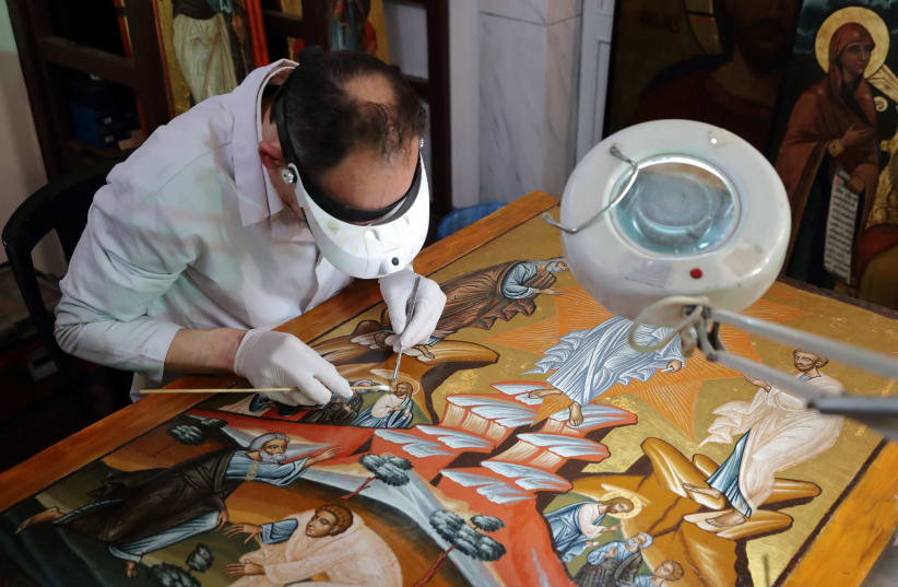 Venizelos Gavrilakis, a senior restorer and conservator from Thessaloniki, Greece, works to clean and restore a 16th century Byzantine Christian icon at a Greek Orthodox church where he set up his laboratory in Istanbul, Turkey January 26, 2021 (photo credit: REUTERS)