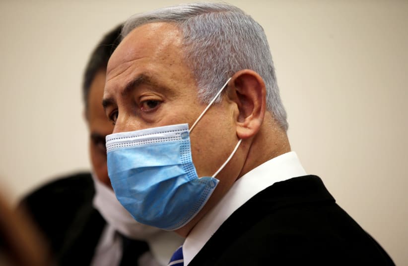 Israeli Prime Minister Benjamin Netanyahu, wearing a face mask, looks on while standing inside the court room as his corruption trial opens at the Jerusalem District Court  May 24, 2020. (photo credit: RONEN ZVULUN/REUTERS)