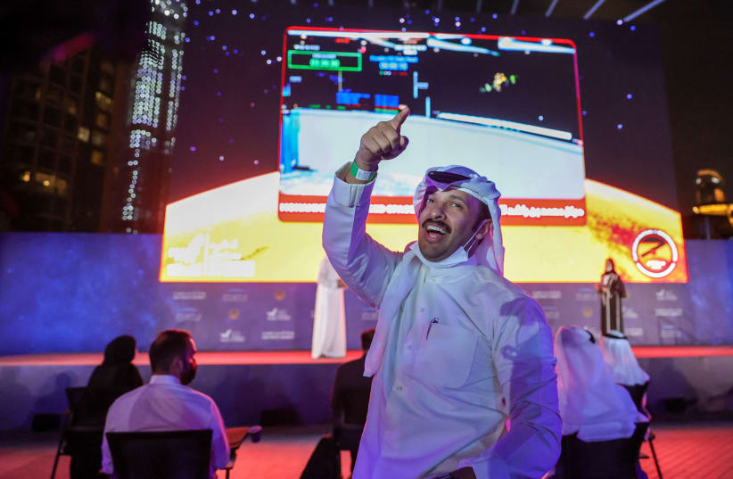 A man gestures as people watch a screen displaying information of the Hope Probe entering the orbit of Mars, in Dubai, United Arab Emirates, February 9, 2021. (photo credit: CHRISTOPHER PIKE/REUTERS)