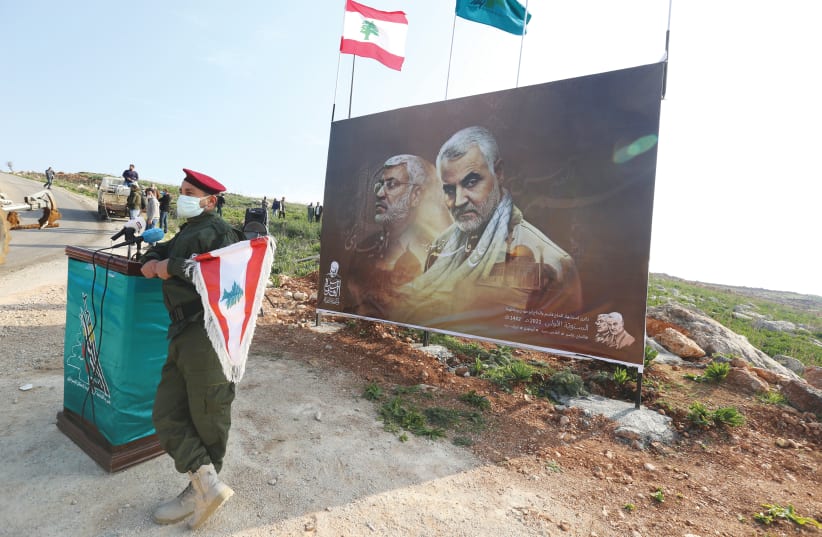 A HEZBOLLAH member holds a Lebanese flag in front of a picture depicting Iranian Gen. Qasem Soleimani and Iraqi militia commander Abu Mahdi al-Muhandis, in Khiam, Lebanon, last month. (photo credit: AZIZ TAHER/REUTERS)