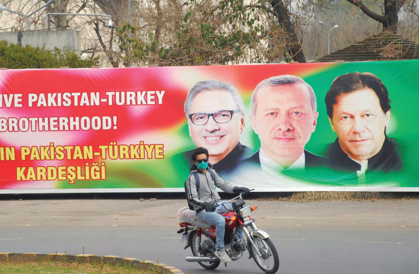 A MAN RIDES his motorbike past a sign showing Pakistan’s President Alvi, Turkey’s President Erdogan and Pakistan’s Prime Minister Khan, in Islamabad, Pakistan, last year. (photo credit: WASEEM KHAN/REUTERS)