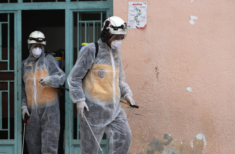 Members of the Syrian Civil defense wear protective gears as they sanitize a school as part of the preventive measures against the spread of the coronavirus, in Afrin, Syria March 18, 2020 (photo credit: REUTERS/KHALIL ASHAWI)