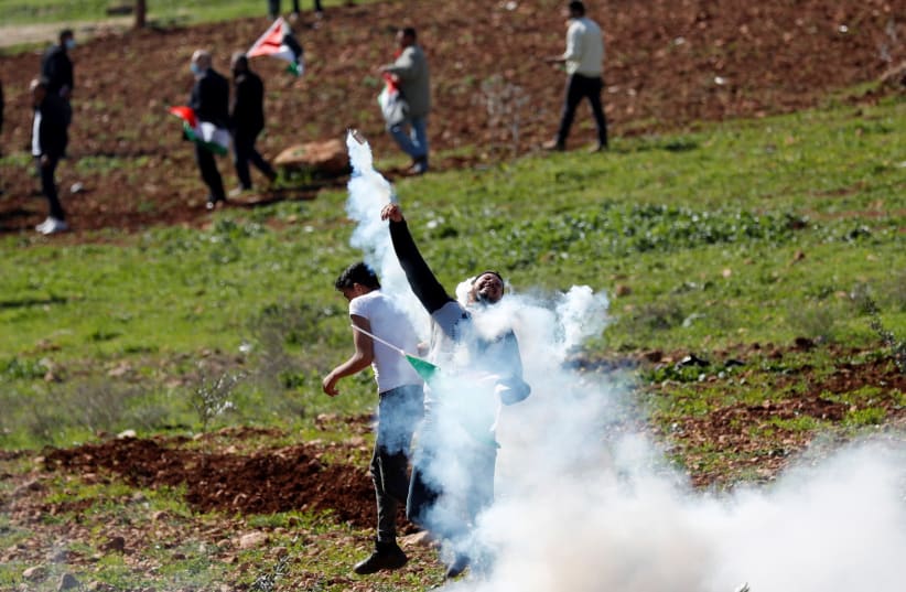 A Palestinian demonstrator returns a tear gas canister fired by Israeli troops during a protest against Israeli settlements, In Beit Dajan in the West Bank February 12, 2021. (photo credit: MOHAMAD TOROKMAN/REUTERS)