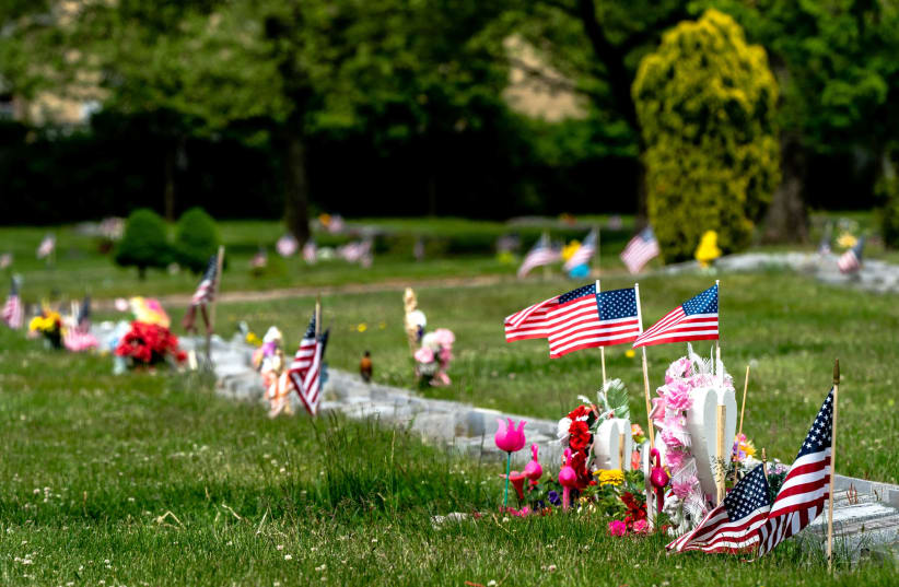 American flags sit on graves during Memorial Day following the outbreak of the coronavirus disease (COVID-19) in the Staten Island borough of New York US, May 25, 2020 (photo credit: JEENAH MOON/REUTERS)