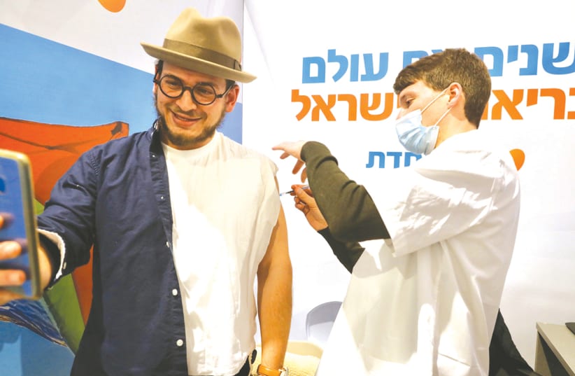 A MAN takes a picture of himself receiving a coronavirus vaccine at a Meuhedet Health Fund center in Jerusalem this week. (photo credit: MARC ISRAEL SELLEM/THE JERUSALEM POST)