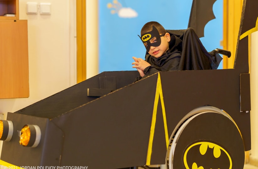 A disabled child is seen wearing a custom batman costume incorporating the wheelchair as a batmobile ahead of Purim. (photo credit: JORDAN POLEVOY)