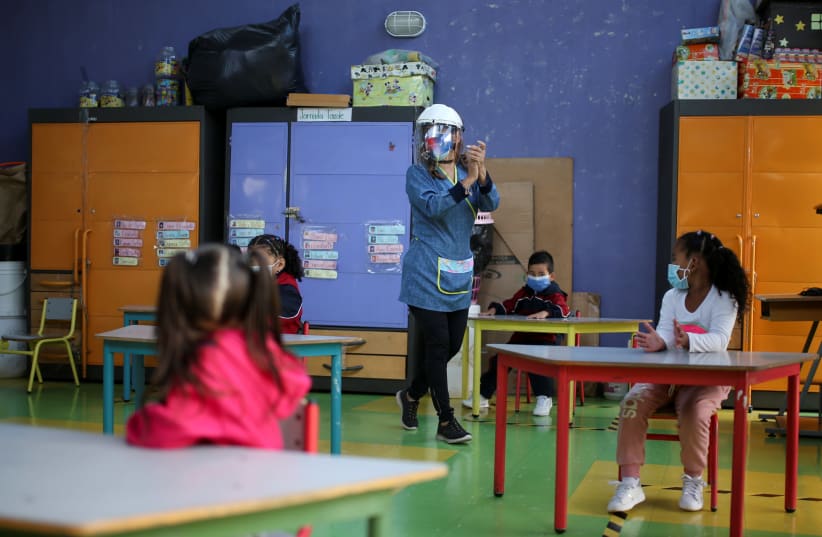 A teacher walks in a classroom with students keeping social distancing in a public school, after the reactivation of face-to-face classes, amidst an outbreak of the coronavirus disease (COVID-19), in Bogota, Colombia February 15, 2021 (photo credit: LUISA GONZALEZ/REUTERS)