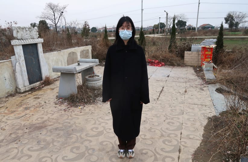 Deng Wei poses for a picture in front of her grandmother's and father's tombs, both of whom died due to complications related to the coronavirus disease (COVID-19), in Wuhan, Hubei province, China January 24, 2021.  (photo credit: REUTERS/MARTIN POLLARD)