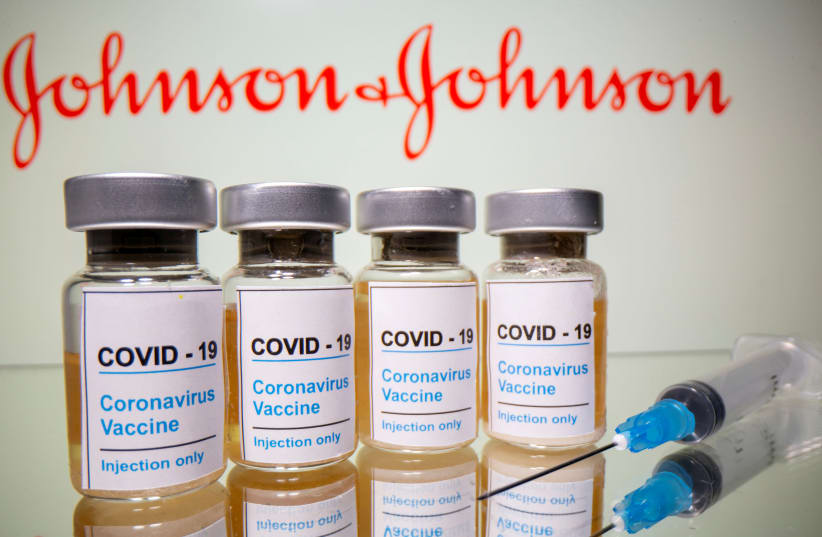 Vials with a sticker reading, "COVID-19 / Coronavirus vaccine/ Injection only" and a medical syringe are seen in front of a displayed Johnson & Johnson logo in this illustration taken October 31, 2020. (photo credit: DADO RUVIC/REUTERS)