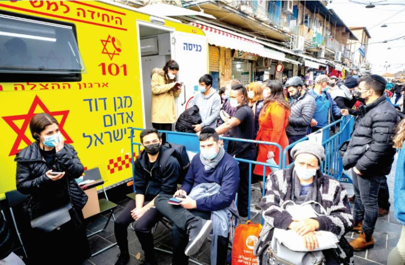 PEOPLE WAIT to receive their COVID-19 vaccine injections outside a mobile Magen David Station at the Mahaneh Yehuda market in Jerusalem, on Monday. (photo credit: OLIVIER FITOUSSI/FLASH90)
